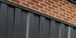 Dark Colorbond fence beside a brick wall